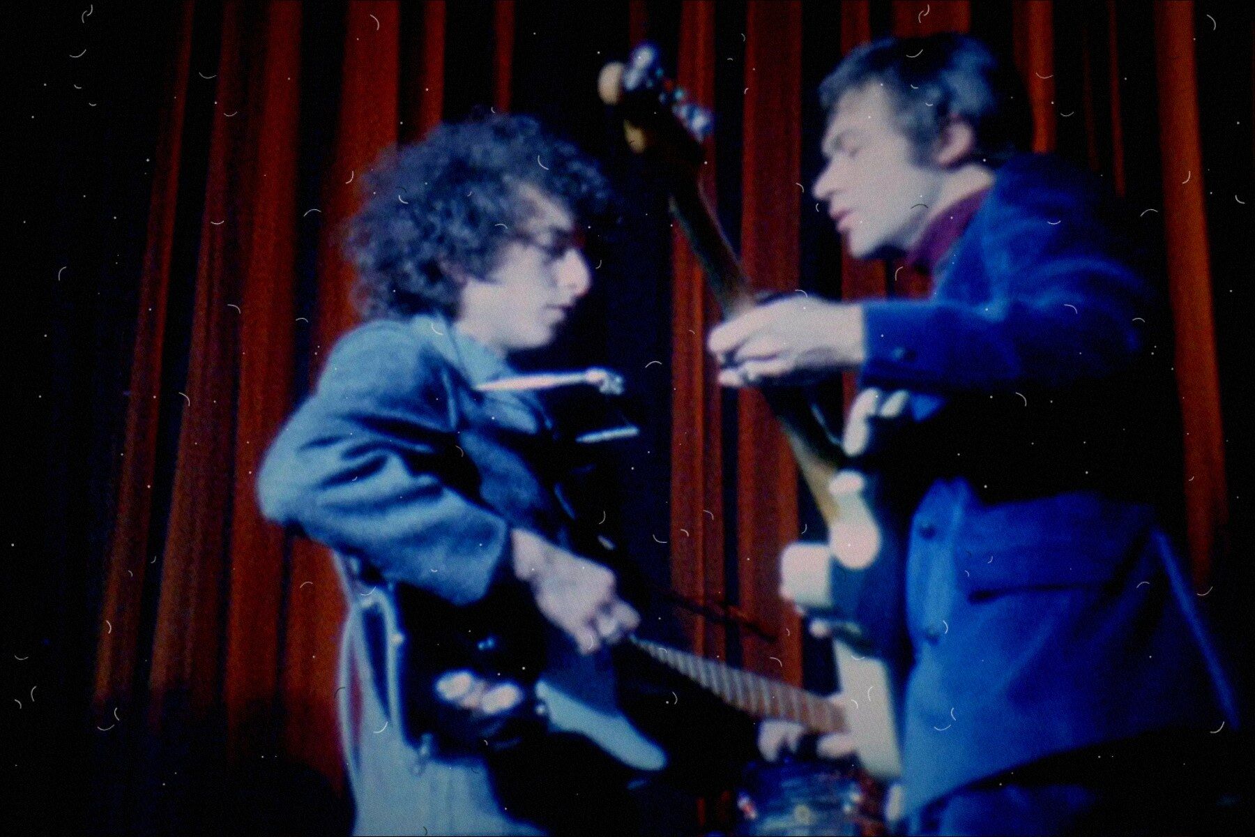 Bob Dylan and a guitarist face to face on stage before a red curtain, 1966
